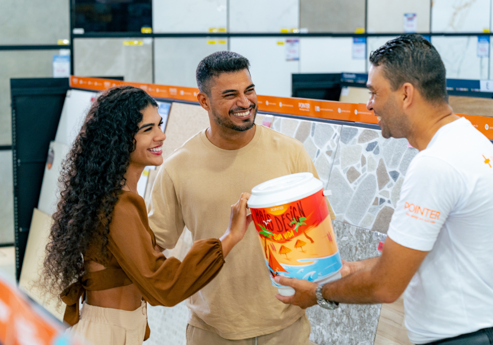 Vendedor oferecendo um brinde a um casal de clientes em uma loja de materiais de construção