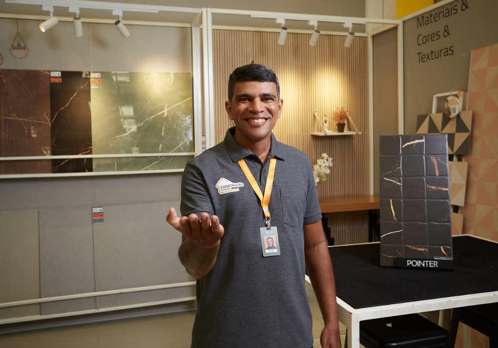 Vendedor sorridente, com a mão direita na direção da câmera, como se convidasse o observador a se aproximar